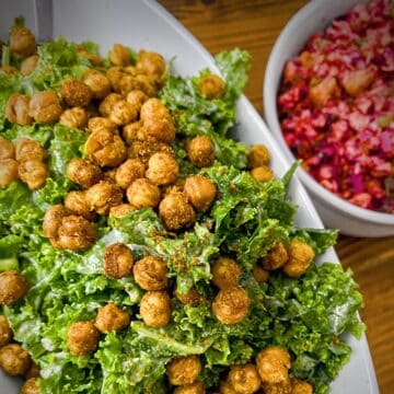 kale salad with tandoori roasted chickpeas in an oblong white dish on a wooden table with a bowl of cranberry relish to the side.