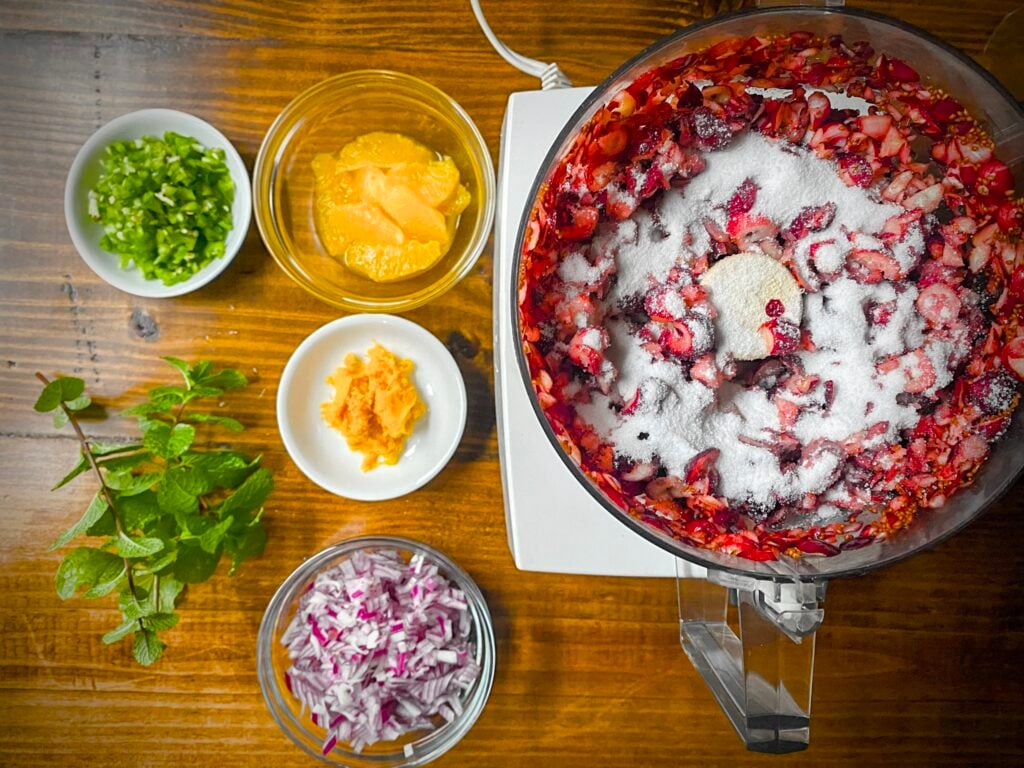 sugar sprinkled on chopped cranberries in bowl of food processor