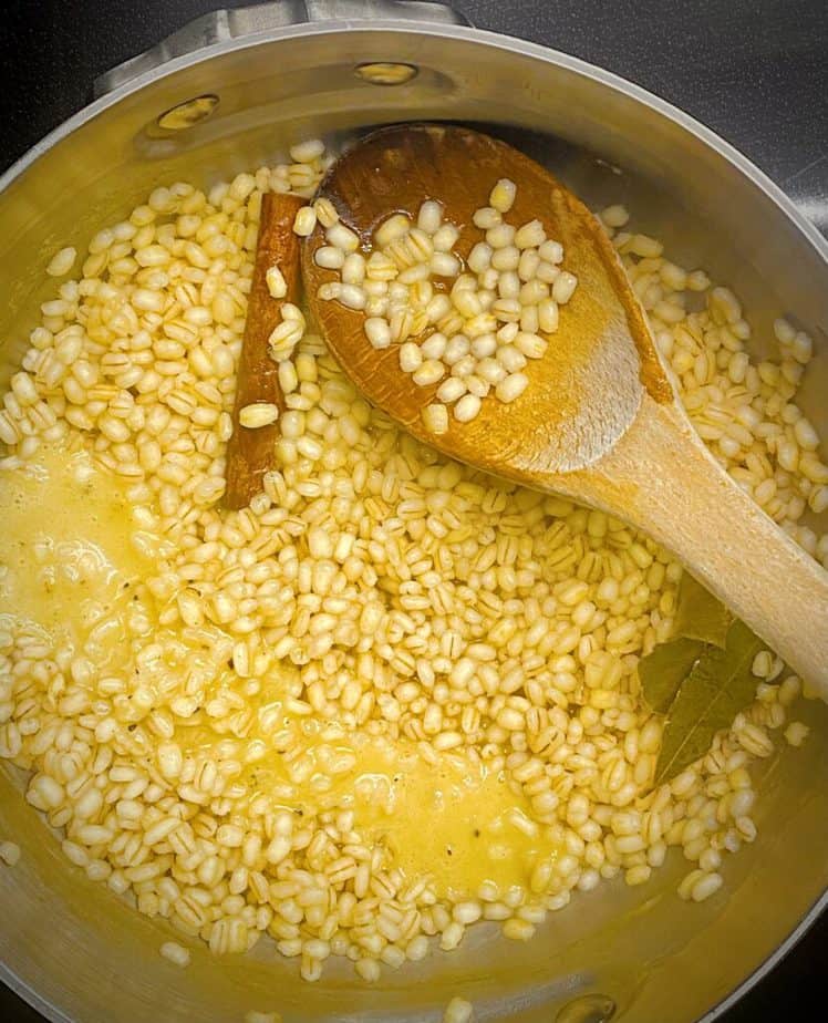 cooked barley in a saucepan with a drizzle of creamy maple vinaigrette with a wooden spoon