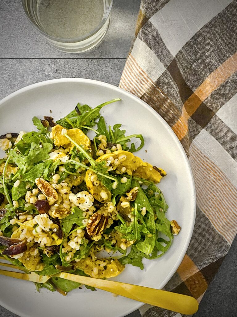 overhead shot of delicata squash harvest salad in a white pasta bowl with a pale orange, brown and white plaid napkin and a glass of white wine