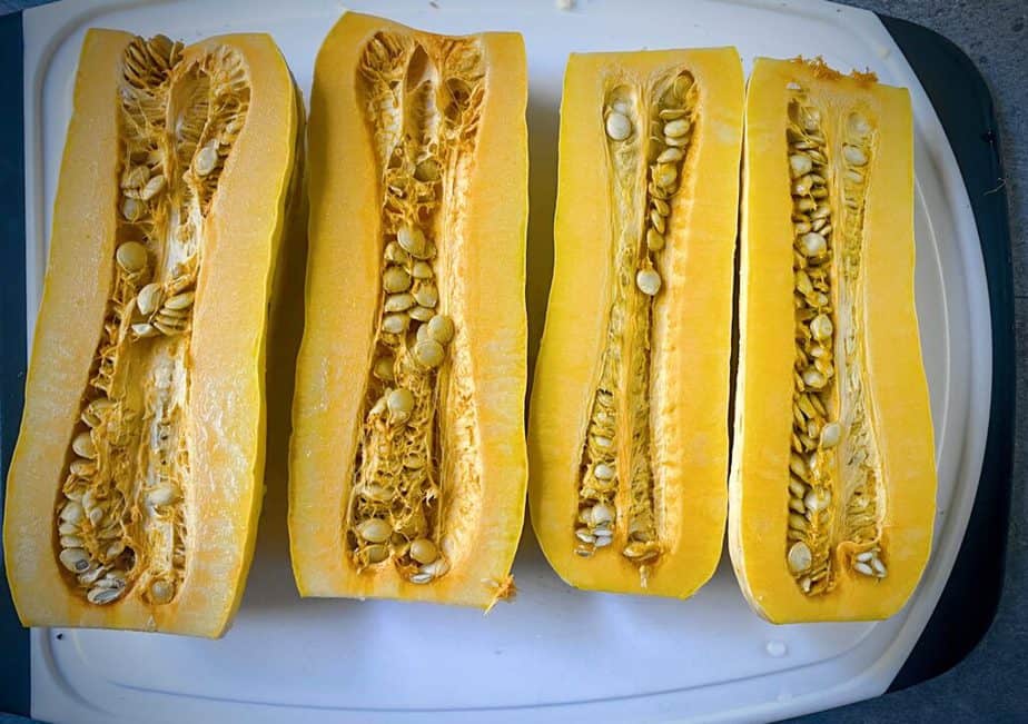 two delicata squash that have had the ends removed and have been cut in half vertically on a white cutting board