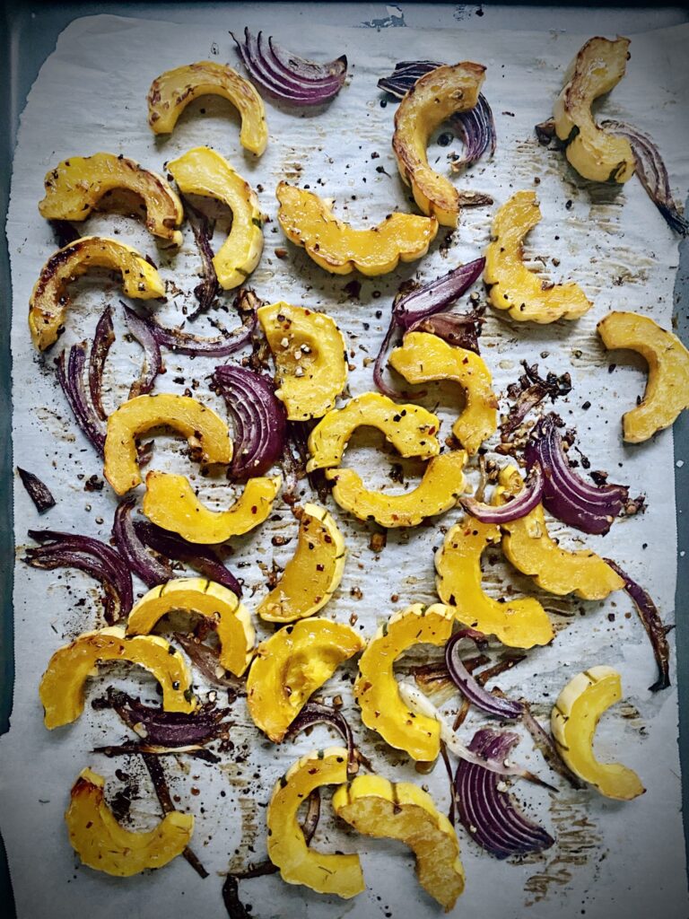 roasted slices of delicata squash and red onion on a parchment lined sheet pan