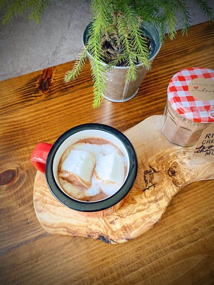 overhead shot of red speckled mug filled with homemade creamy hot chocolate and homemade marshamallows on a slab of olive wood