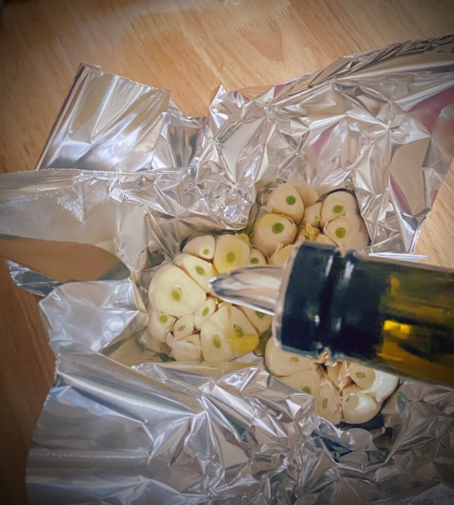 three heads of garlic in foil being drizzled with olive oil