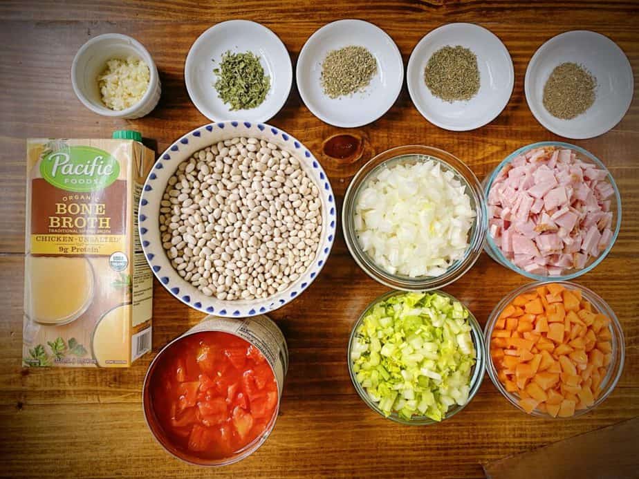 dried navy beans, mirepoix, garlic, ham, canned tomatoes, bone broth, basil, oregano, thyme and parsley as mis en place for instant pot navy bean soup recipe.