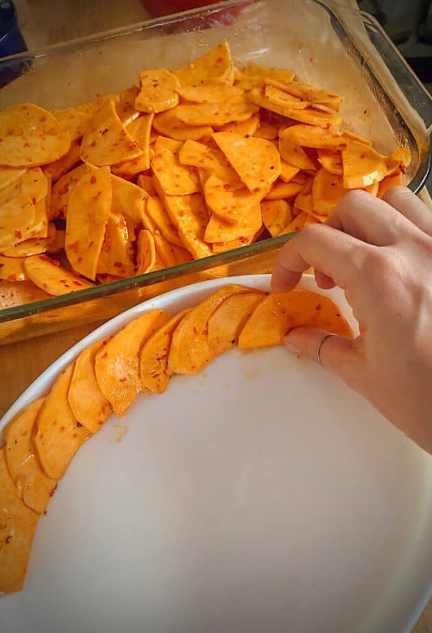 hand arranging sweet potato slices in an oblong white roasting dish to make a tian