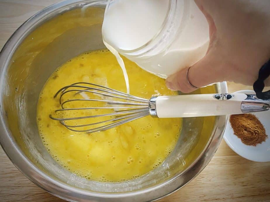 hand pouring milk into whisked eggs