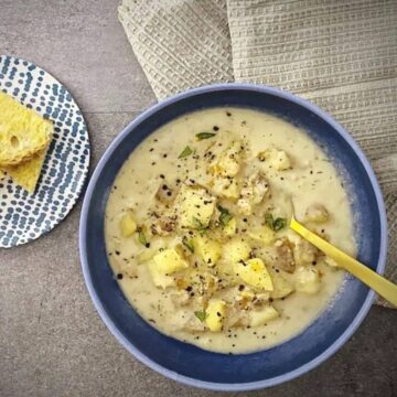 close up shot of clam chowder in a blue bowl with a plate of buttered toast.
