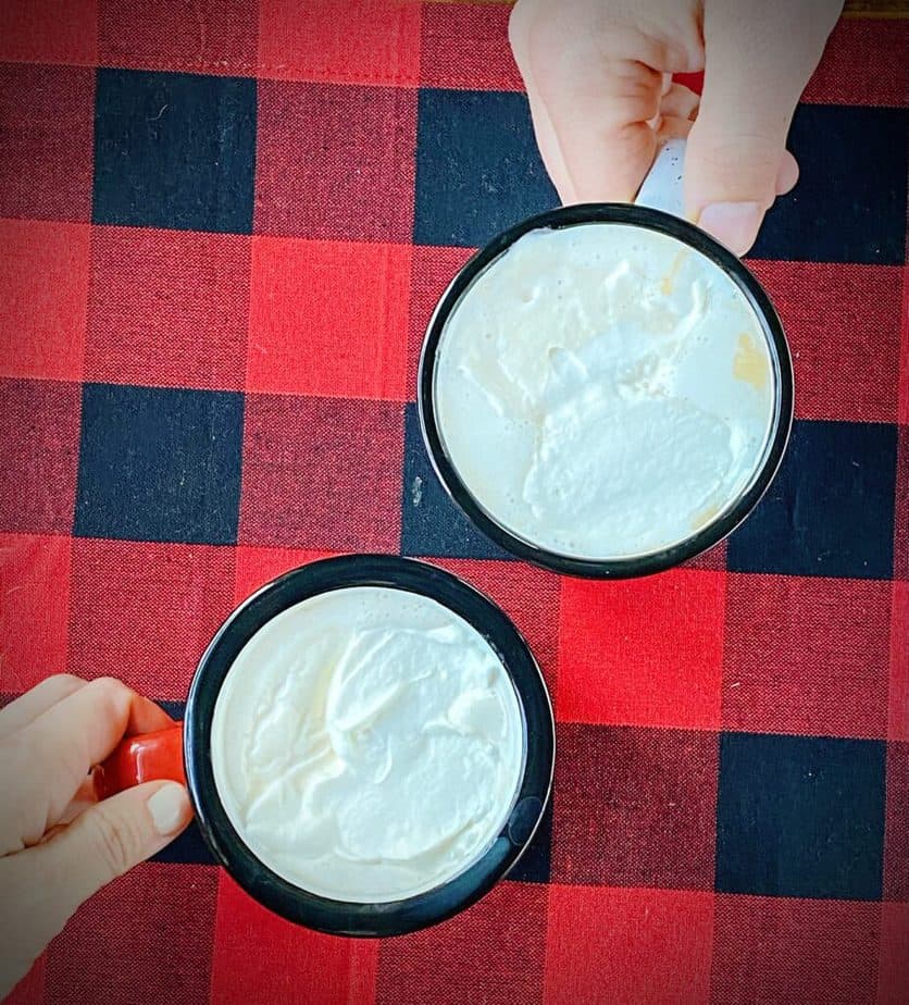 two hands grabbing for thick enamel mugs filled with christmas coffee on a red and black buffalo check table