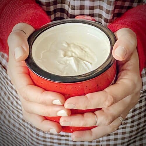 woman holding a mug of amaretto whipped cream topped christmas coffee in a red mug