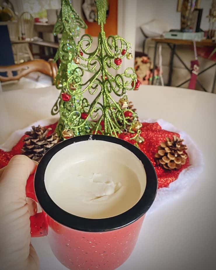 hand holding red mug of christmas coffee in front of a christmas decorated white tulip table