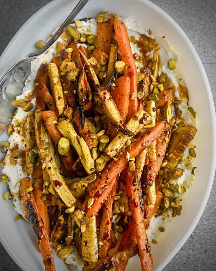 hero shot of sumac roasted carrots and parsnips on a bed of whipped feta and topped with pistachios and pomegranate molasses