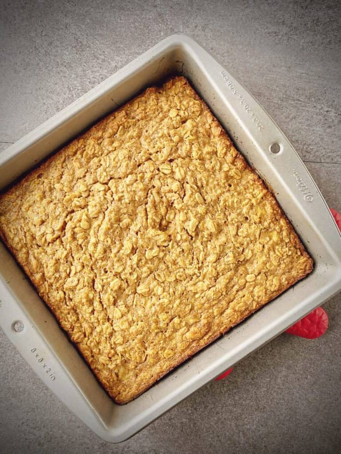 completed square tin of banana baked oatmeal on a red trivet on a grey table