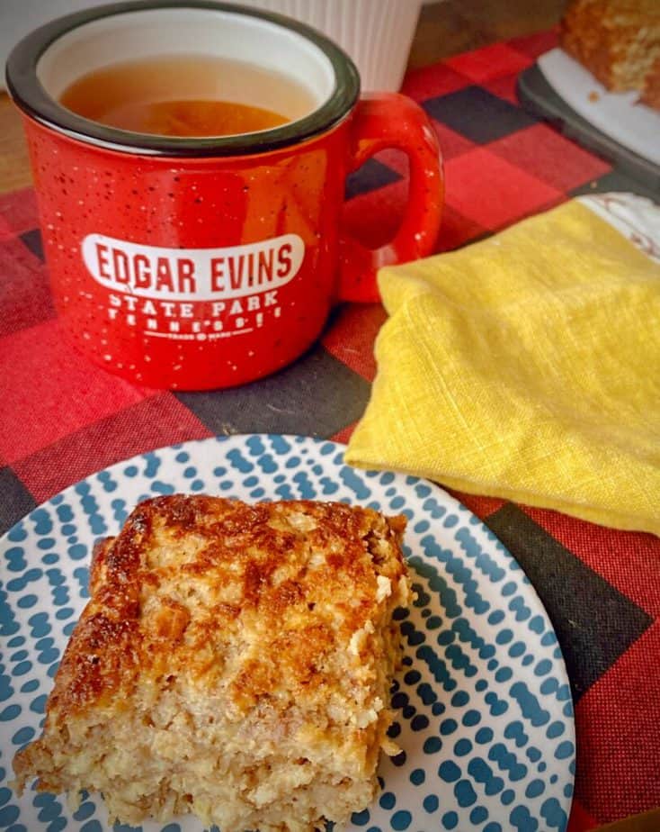square of banana nut butter baked oatmeal on a blue and white plate with a yellow napkin and a red speckled mug of tea