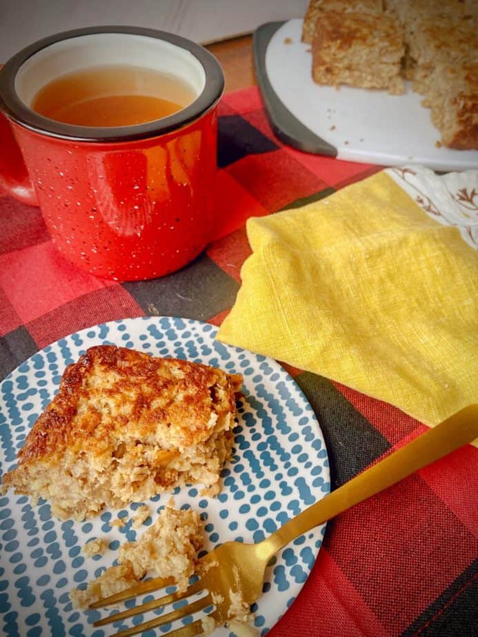 slice of banana baked oatmeal on a blue and white dessert plate with a gold fork, a mustard yellow napkin and a red mug of team on a black and red buffalo check tablecloth