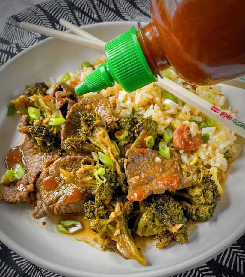 bottle of sriracha being drizzled onto completed plate of broccoli beef with fried rice