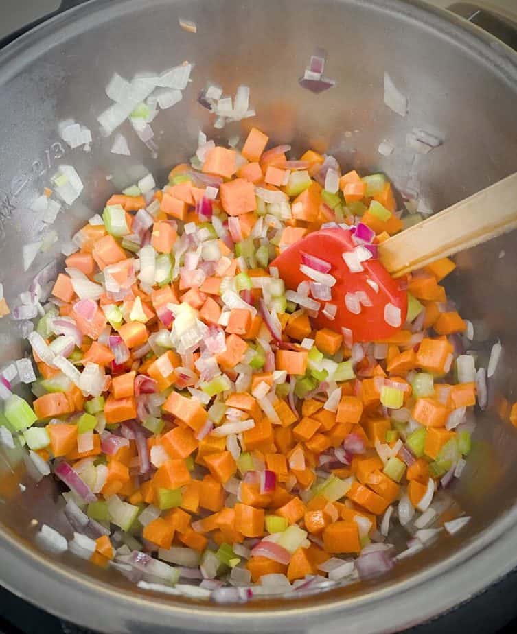 sautéed carrots, onions and celery in the metal insert of the instant pot with a red silicone spatula