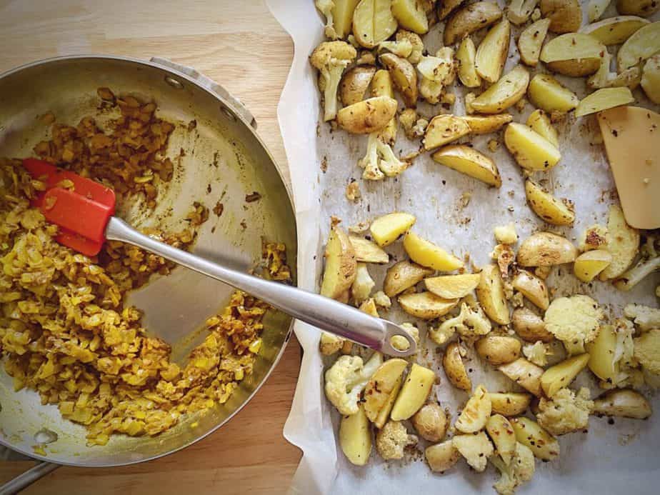 aloo gobi sauce in sauté pan next to sheet pan of roasted cauliflower and potatoes