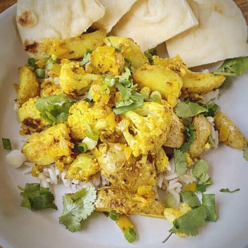 aloo gobi over cumin scented rice with wedges of toasted naan in a white pasta bowl