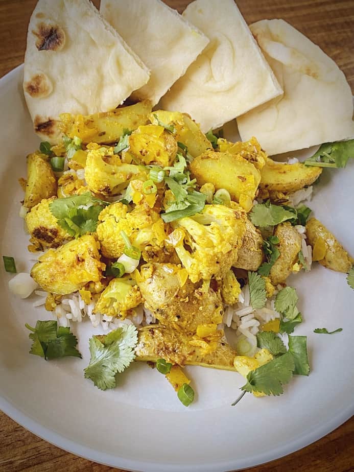 aloo gobi over cumin scented rice with wedges of toasted naan in a white pasta bowl