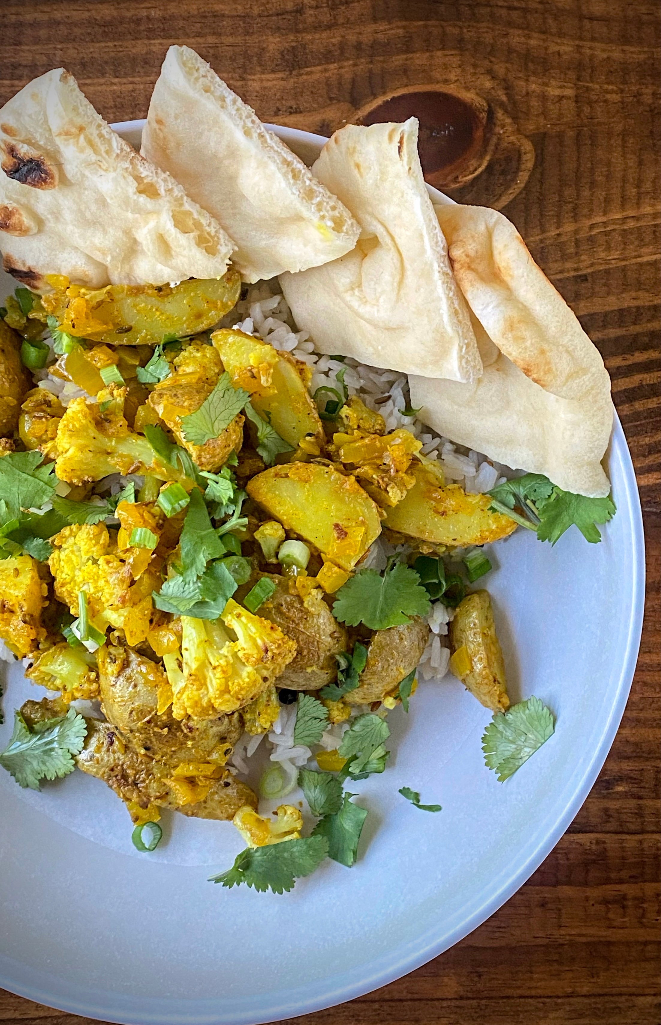 aloo gobi over cumin rice with sliced naan in a white pasta bowl on a wooden table