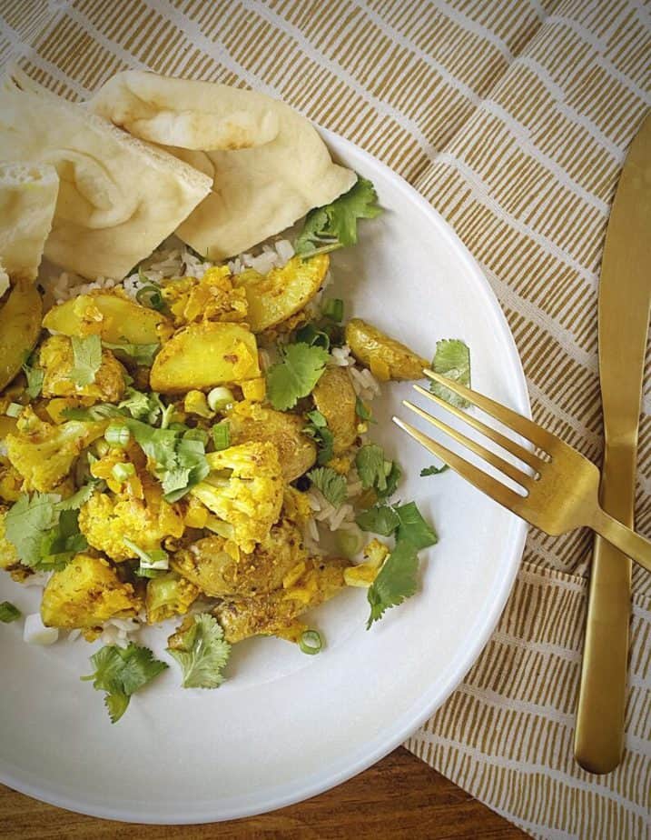 aloo gobi in a white pasta bowl on a gold and white striped linen