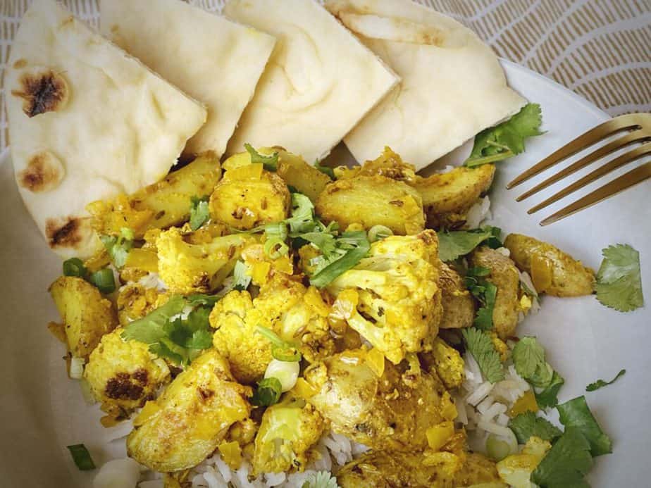 aloo gobi with rice and naan in a white pasta bowl with a gold fork