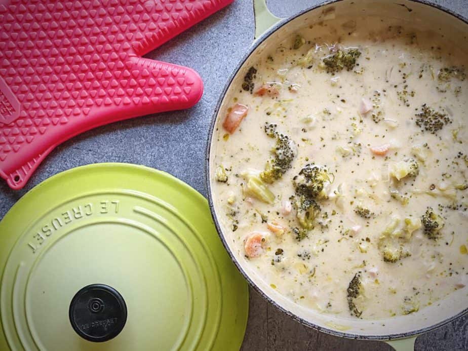 overhead shot of completed broccoli cheddar soup in a light green le creuset dutch oven on a grey table