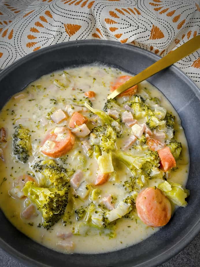final shot of broccoli cheese chowder in grey pasta bowl with gold spoon