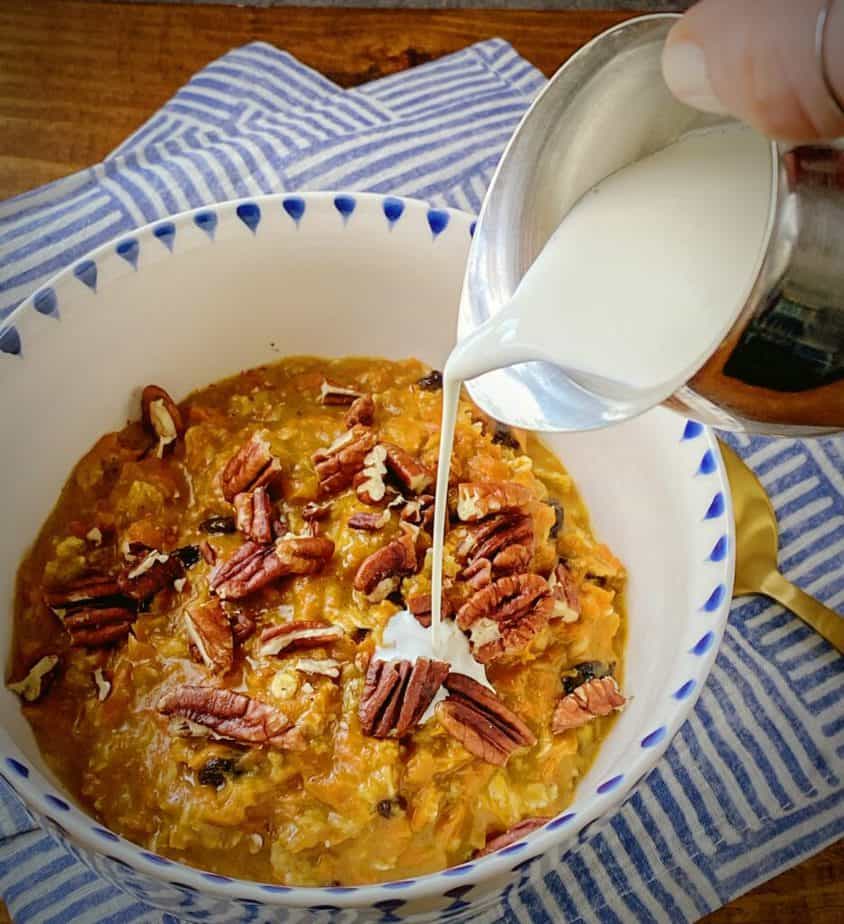 hand holding a silver creamer dish pouring heavy cream onto bowl of carrot cake oatmeal