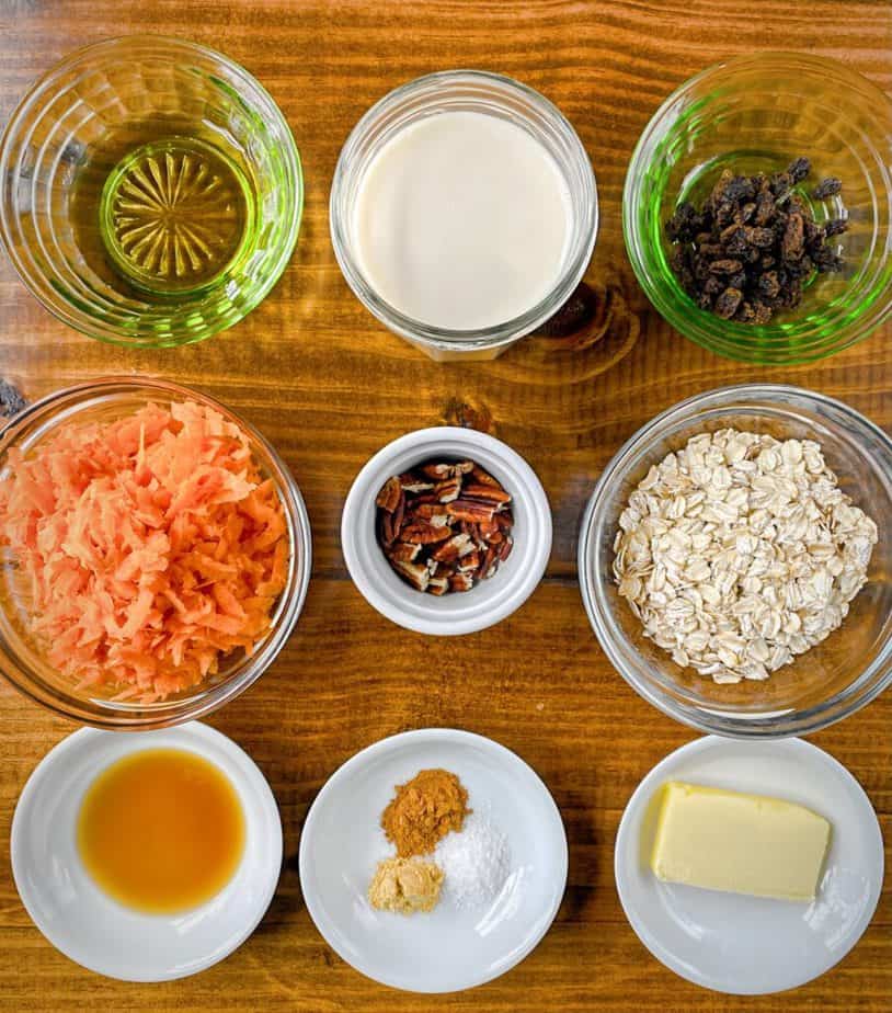 mise en place for carrot cake oatmeal recipes - agave, soy milk, raisins, shredded carrot, rolled oats, vanilla, ground cinnamon, ground ginger, kosher salt and butter all in small bowls