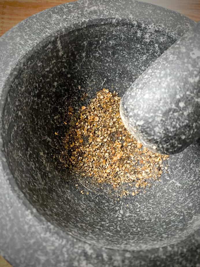 coriander and black peppercorns after being pulverized in a mortar and pestle 