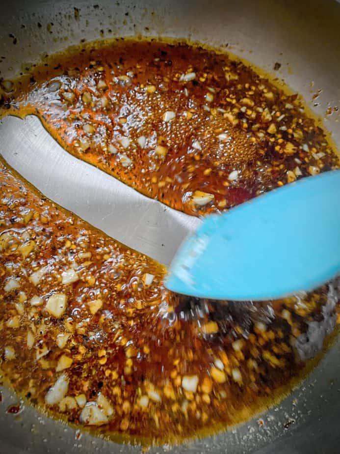 blue silicone spatula pulling across kung pao sauce in sauté pan, showing a clean bottom. this indicates the sauce is ready.
