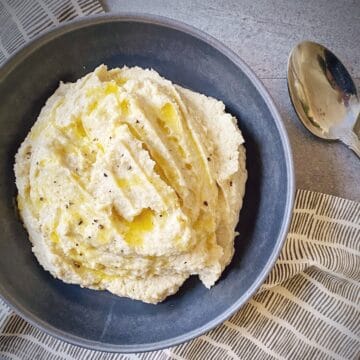 mashed cauliflower in a grey pasta bowl drizzled with melted butter.