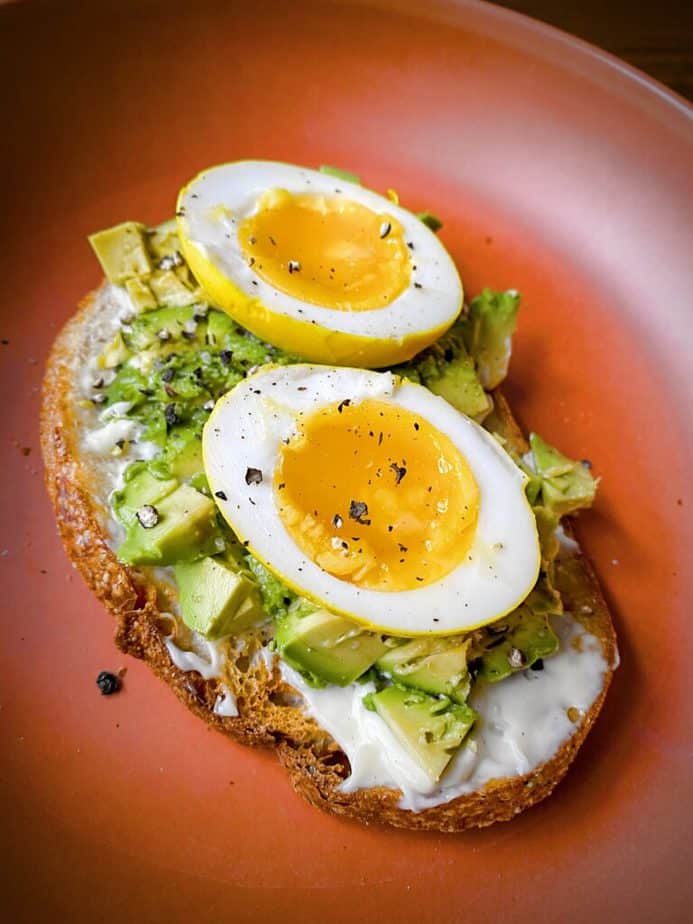 45 degree angle shot of halved turmeric pickled egg on avocado toast to show bright yellow exterior