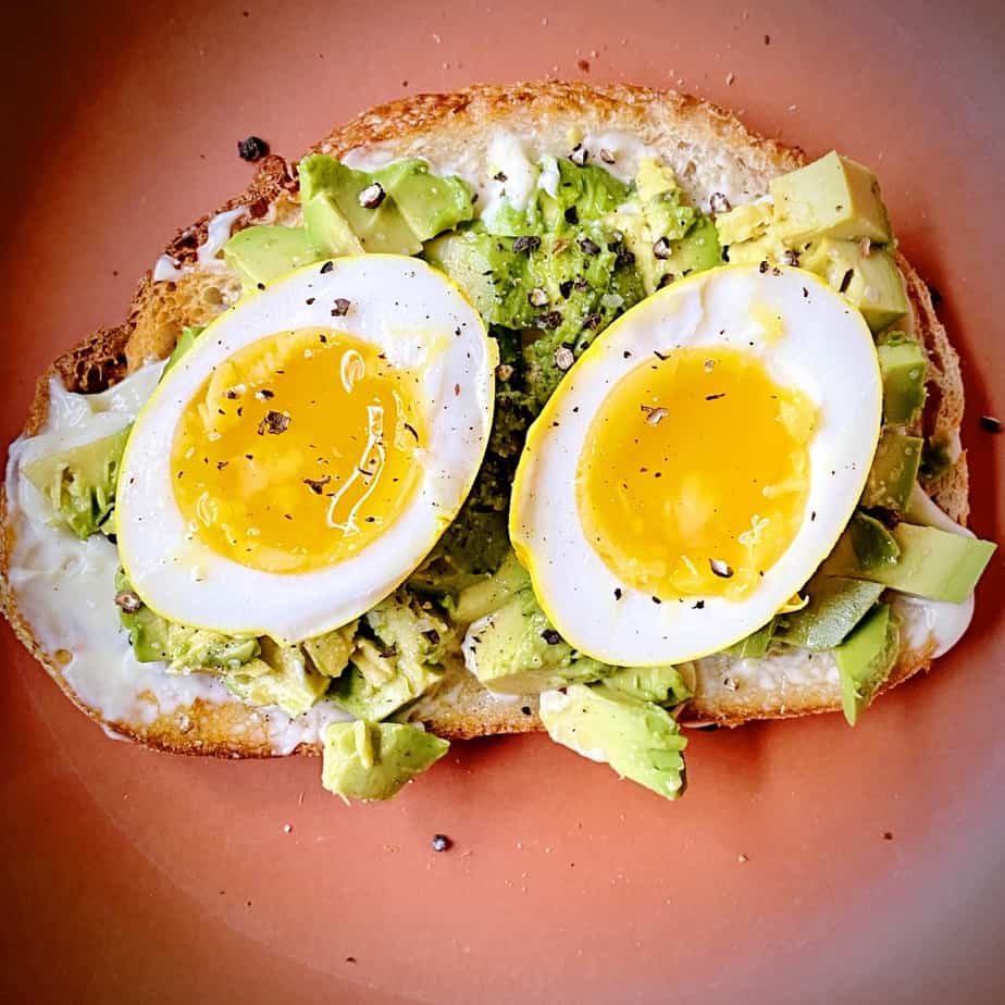 overhead close up shot of halved turmeric pickled egg on avocado toast