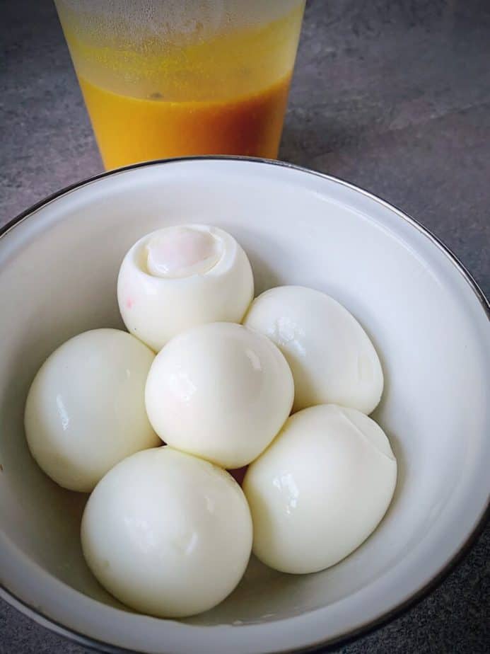 peeled 7 minute eggs in a bowl with a delitainer of turmeric pickling liquid 