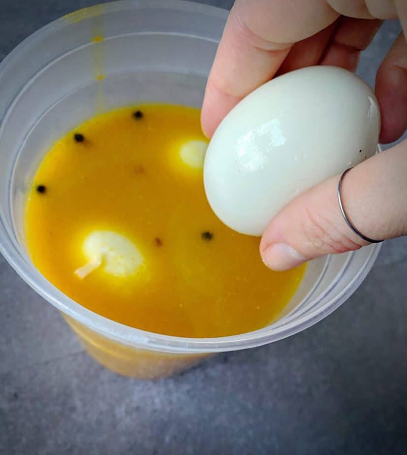 hand holding peeled 7 minute egg above delitainer of turmeric pickling brine