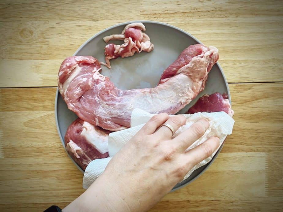 hand blotting pork tenderloin with a paper towel