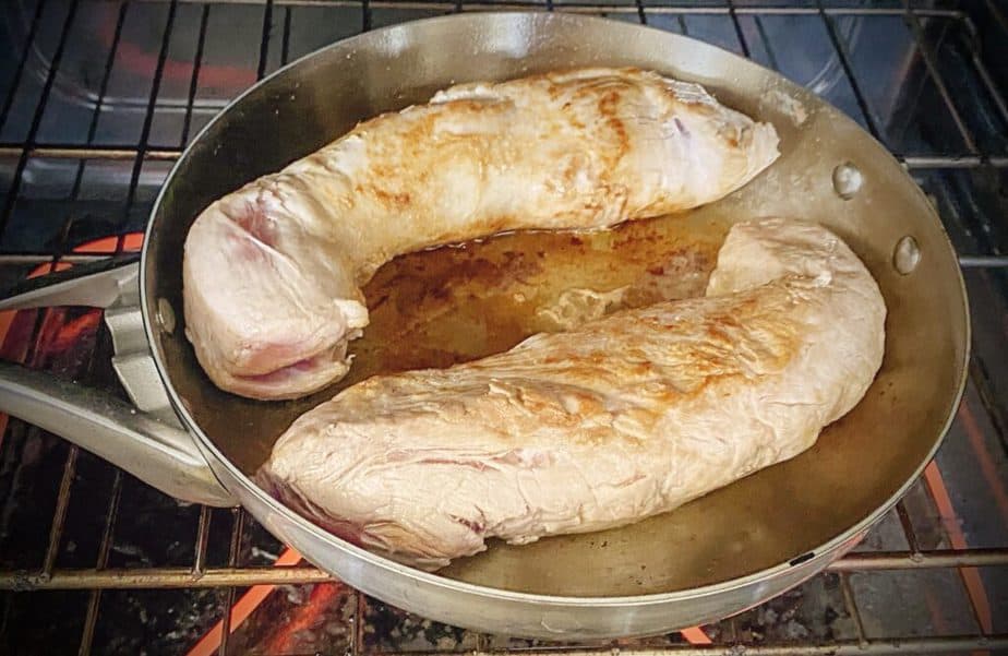 two seared pork tenderloins in a skillet in a hot oven to roast