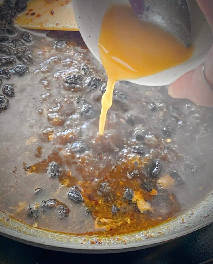 hand pouring cornstarch slurry into ginger raisin pan sauce
