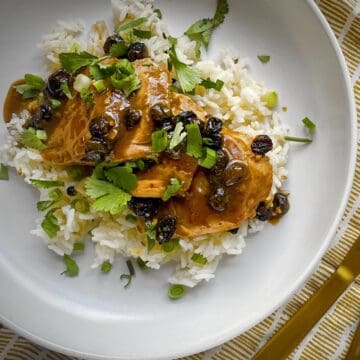slices of roasted pork tenderloin with ginger raisin pan sauce over a bed of rice in a white bowl.