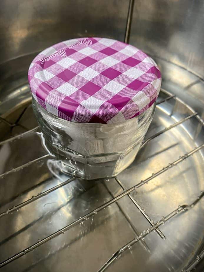 small glass jar with purple and gingham lid filled with cbd flower in the instant pot to decarb