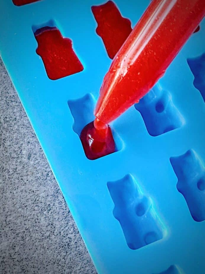 close up shot of dropper filling a gummy bear mould with cbd jello mixture