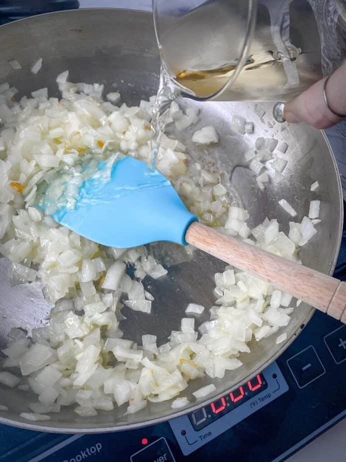 hand pouring in glass of white wine into sauté pan with onions