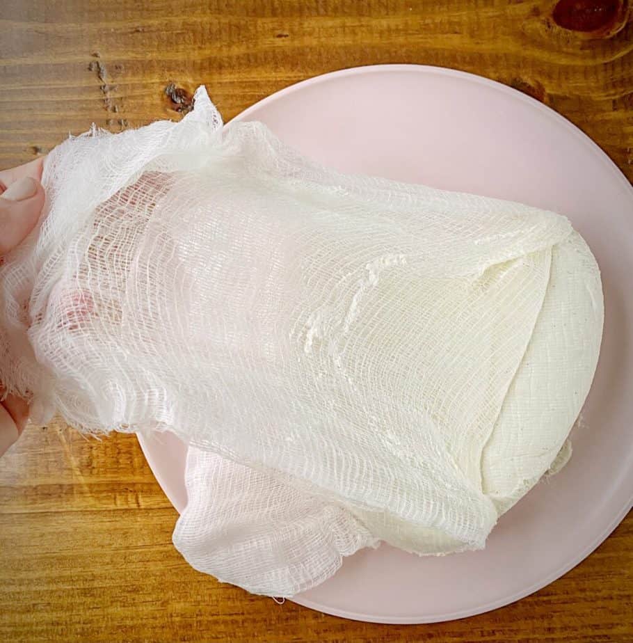 hand peeling off cheesecloth from coeur à la crème