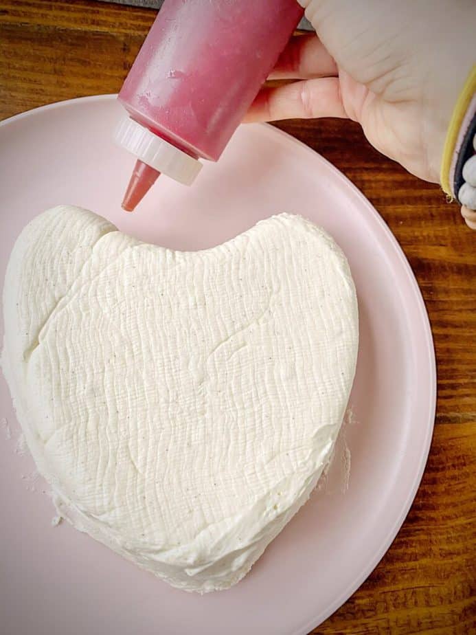 hand holding a squeeze bottle of raspberry amaretto sauce to decorate unmoulded coeur a la creme