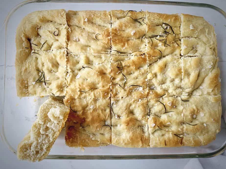 overhead shot of tray of rosemary focaccia with one slice removed and turned on its side to show texture