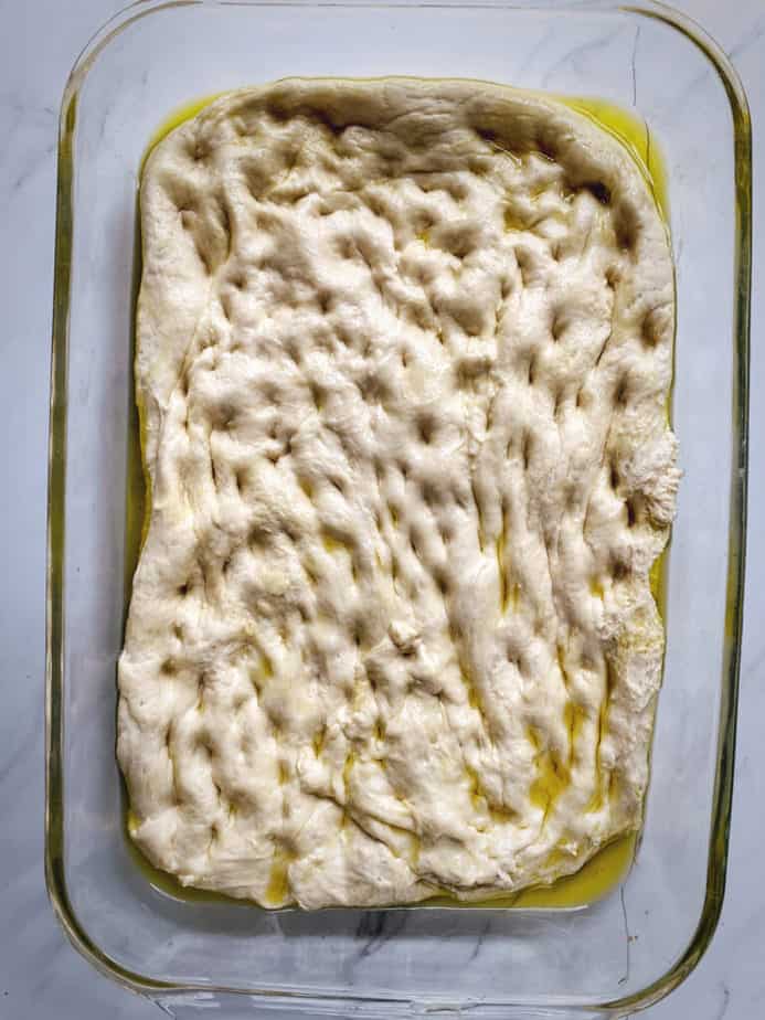 9x13 pyrex baking dish with focaccia dough that has been stretched out for second rise