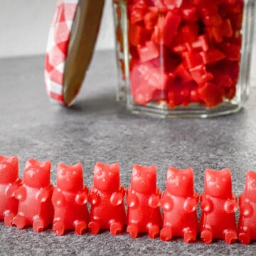 red homemade THC CBD gummy bears lined up in a row with a jar of them in the background.